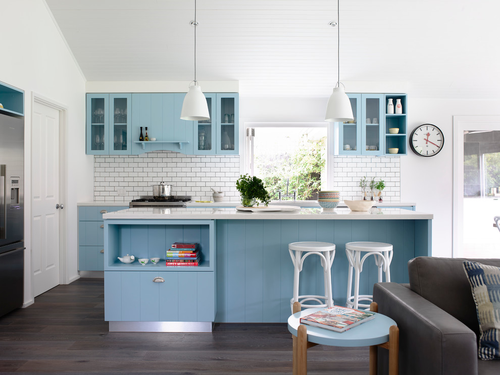 Example of a beach style single-wall open concept kitchen design in Melbourne with blue cabinets, quartz countertops, white backsplash, subway tile backsplash, stainless steel appliances, flat-panel cabinets and an island