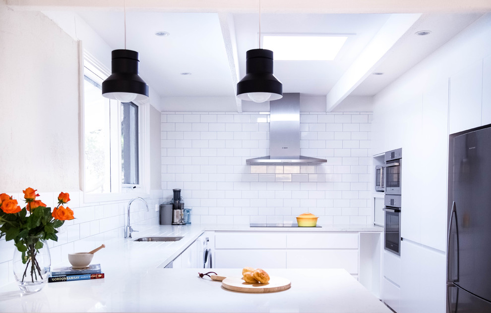 Immagine di una cucina minimalista di medie dimensioni con lavello da incasso, ante bianche, top in superficie solida, paraspruzzi bianco, paraspruzzi con piastrelle diamantate e elettrodomestici in acciaio inossidabile