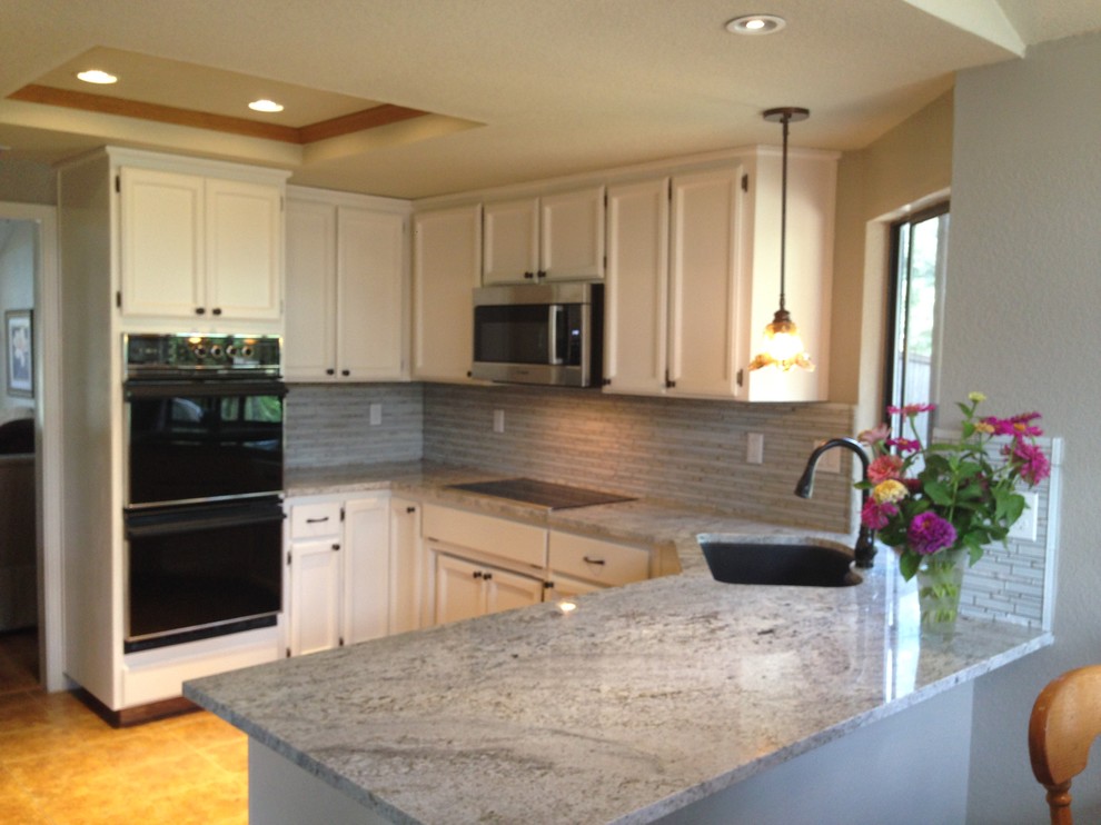 Example of a small beach style u-shaped ceramic tile eat-in kitchen design in Sacramento with recessed-panel cabinets, white cabinets, granite countertops, gray backsplash, glass sheet backsplash, stainless steel appliances and an undermount sink