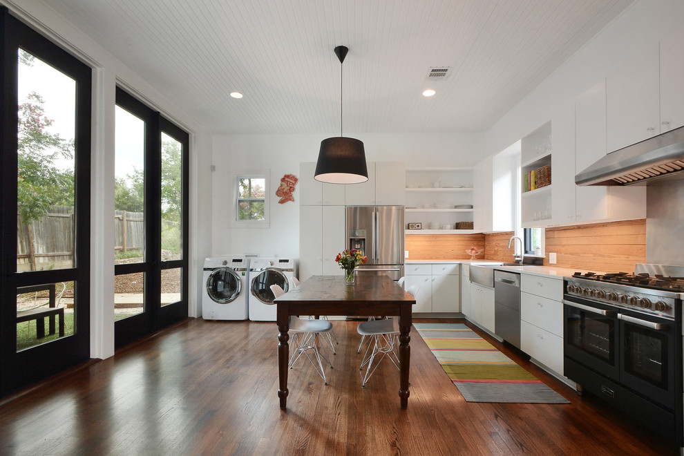 Moderne Küche in L-Form mit Landhausspüle, flächenbündigen Schrankfronten, weißen Schränken, Küchengeräten aus Edelstahl, dunklem Holzboden und Kücheninsel in Austin