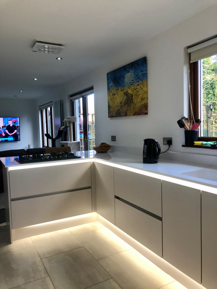 Design ideas for a medium sized contemporary l-shaped open plan kitchen in Glasgow with an integrated sink, flat-panel cabinets, white cabinets, granite worktops, white splashback, black appliances, vinyl flooring, a breakfast bar and white worktops.