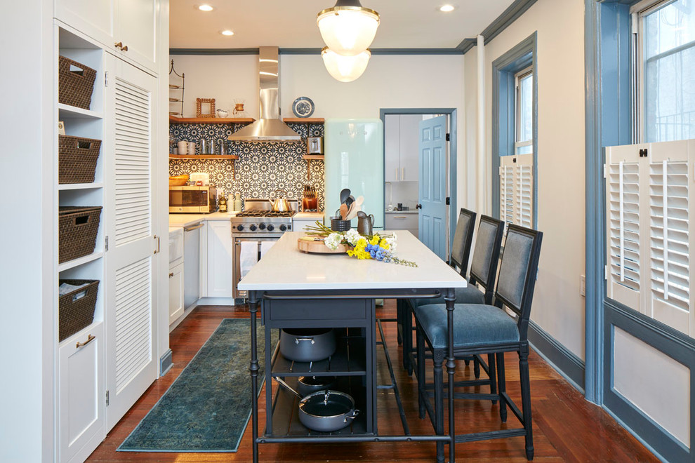 Mid-sized eclectic l-shaped medium tone wood floor and brown floor open concept kitchen photo in New York with a farmhouse sink, shaker cabinets, white cabinets, quartz countertops, multicolored backsplash, cement tile backsplash, stainless steel appliances, an island and gray countertops
