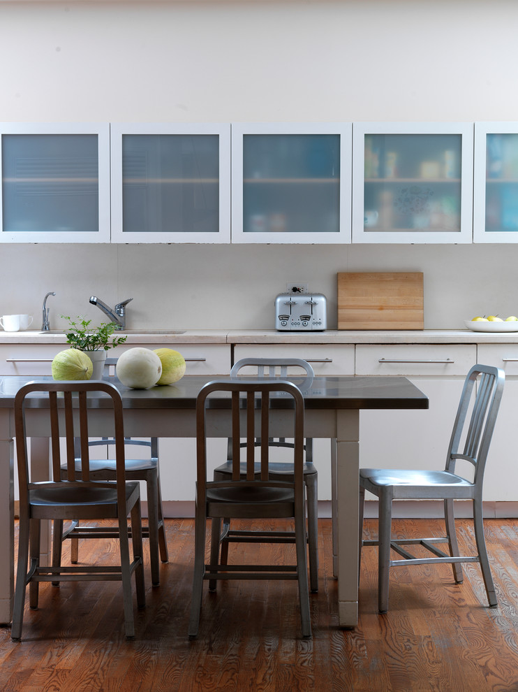 Example of a trendy dark wood floor eat-in kitchen design in New York with an undermount sink, glass-front cabinets and white cabinets
