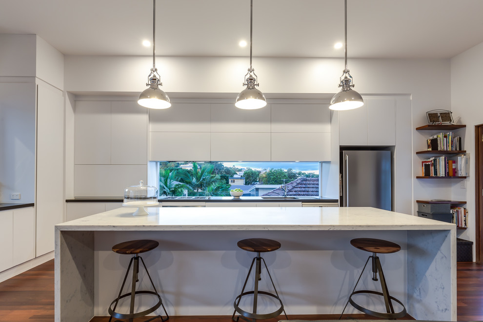 Bild på ett mellanstort funkis linjärt kök med öppen planlösning, med vita skåp, marmorbänkskiva, rostfria vitvaror, en köksö, släta luckor, en undermonterad diskho, fönster som stänkskydd och mellanmörkt trägolv