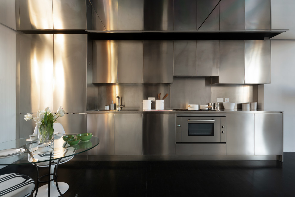 Foto på ett mellanstort funkis grå linjärt kök och matrum, med en dubbel diskho, släta luckor, skåp i rostfritt stål, bänkskiva i rostfritt stål, stänkskydd med metallisk yta, rostfria vitvaror, mörkt trägolv och svart golv