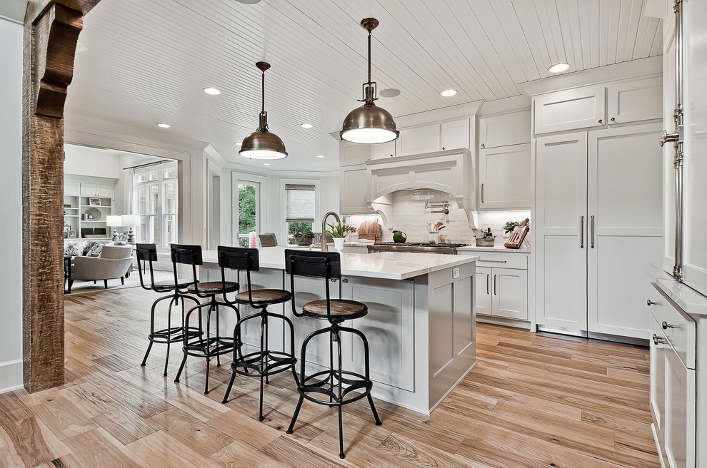 Inspiration for a large farmhouse l-shaped enclosed kitchen in Other with a belfast sink, white cabinets, quartz worktops, white splashback, stone tiled splashback, stainless steel appliances, an island, brown floors, white worktops, recessed-panel cabinets and medium hardwood flooring.