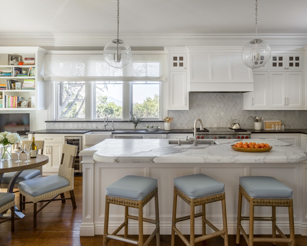 Klassisk inredning av ett u-kök, med en undermonterad diskho, luckor med infälld panel, vita skåp, vitt stänkskydd, rostfria vitvaror, mellanmörkt trägolv, en köksö och brunt golv
