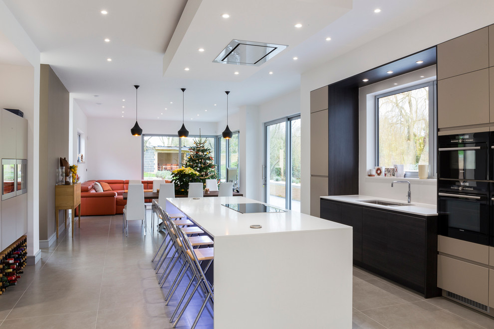 This is an example of a contemporary open plan kitchen in London with a submerged sink, composite countertops, metallic splashback, mirror splashback, black appliances, ceramic flooring and an island.