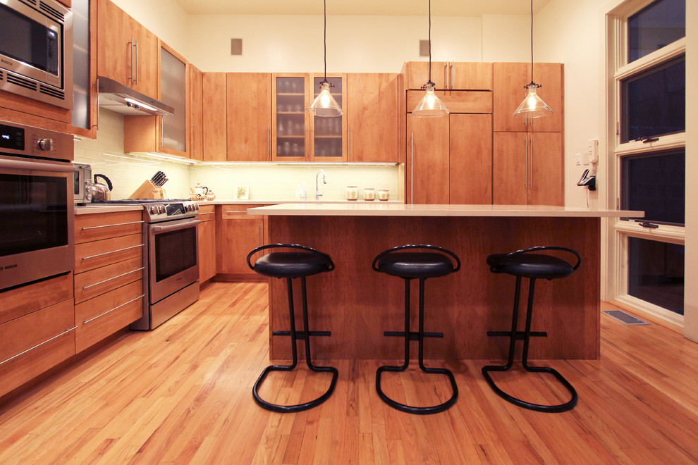 フィラデルフィアにある高級な広いモダンスタイルのおしゃれなキッチン (アンダーカウンターシンク、フラットパネル扉のキャビネット、中間色木目調キャビネット、珪岩カウンター、黄色いキッチンパネル、ガラスタイルのキッチンパネル、シルバーの調理設備、無垢フローリング、茶色い床、白いキッチンカウンター) の写真