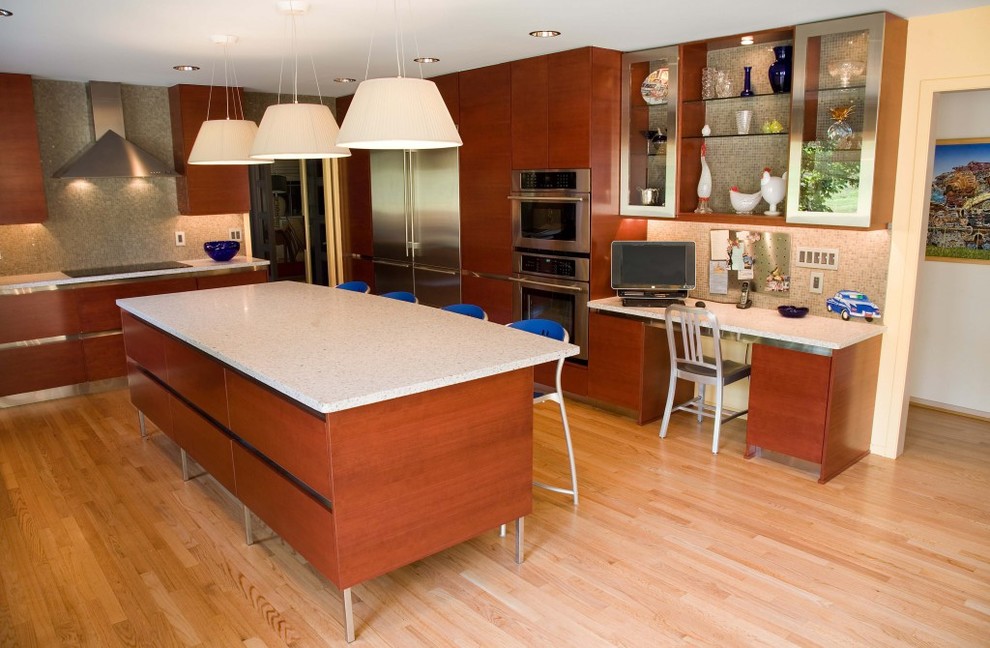 Large contemporary l-shaped kitchen/diner in Detroit with a submerged sink, flat-panel cabinets, medium wood cabinets, engineered stone countertops, beige splashback, ceramic splashback, stainless steel appliances, light hardwood flooring and an island.