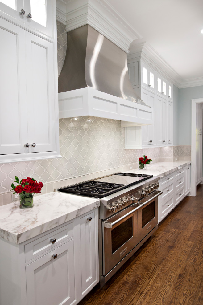Photo of an expansive classic l-shaped kitchen/diner in Detroit with a submerged sink, beaded cabinets, white cabinets, engineered stone countertops, multi-coloured splashback, ceramic splashback, stainless steel appliances, dark hardwood flooring, an island, brown floors and white worktops.