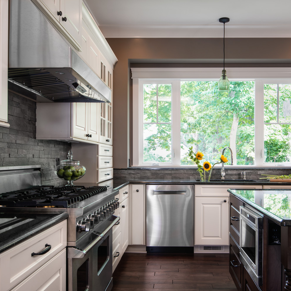 Exempel på ett stort klassiskt l-kök, med en undermonterad diskho, luckor med upphöjd panel, vita skåp, granitbänkskiva, grått stänkskydd, rostfria vitvaror, mörkt trägolv, en köksö och stänkskydd i skiffer