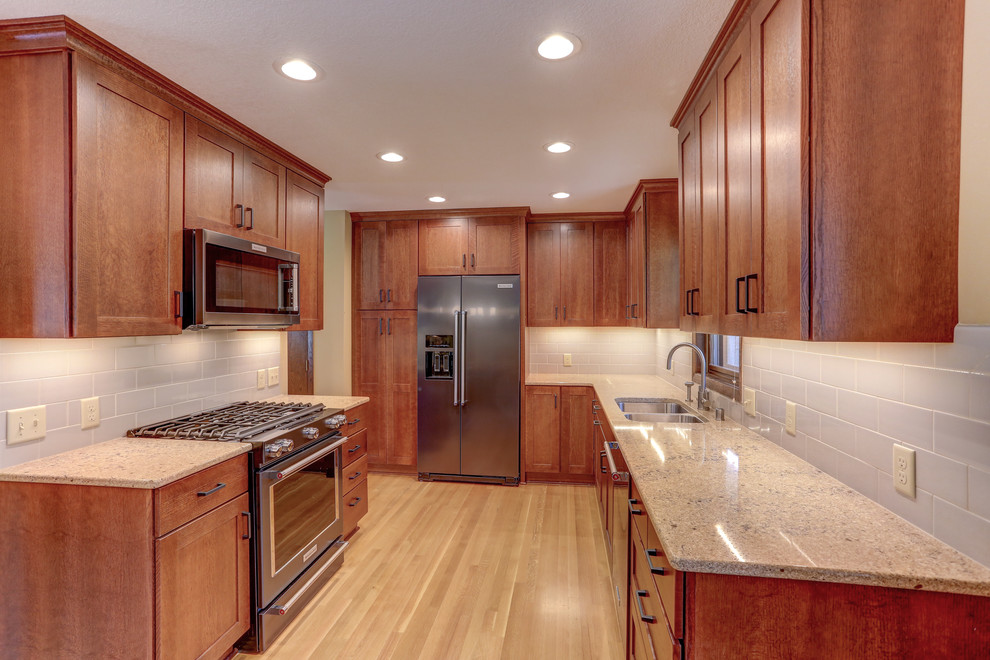 Exempel på ett litet klassiskt grå grått u-kök, med en dubbel diskho, skåp i shakerstil, skåp i mellenmörkt trä, granitbänkskiva, grått stänkskydd, stänkskydd i tunnelbanekakel, rostfria vitvaror, ljust trägolv och beiget golv