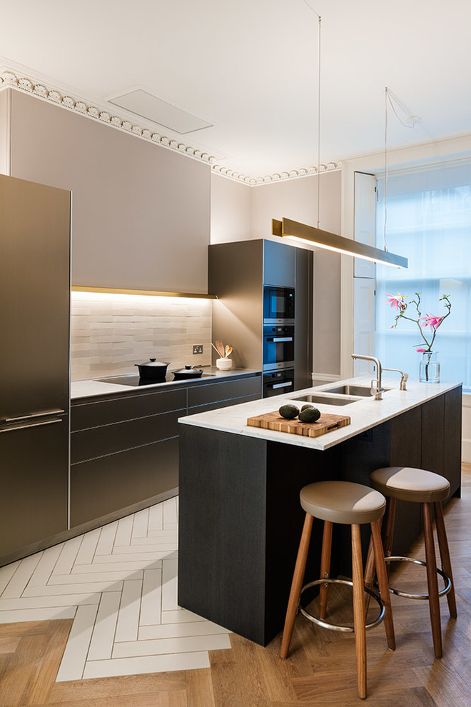 Inspiration for a medium sized contemporary galley kitchen in London with a double-bowl sink, black cabinets, composite countertops, flat-panel cabinets, white splashback, stainless steel appliances, an island and white floors.