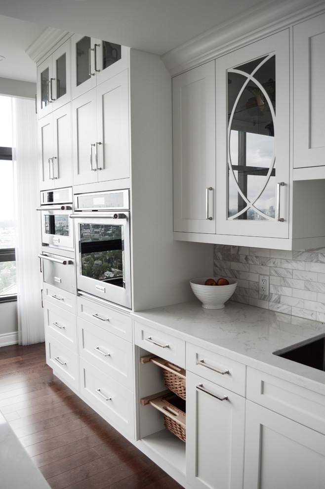 Inspiration for a large transitional l-shaped medium tone wood floor eat-in kitchen remodel in Toronto with an undermount sink, shaker cabinets, white cabinets, quartz countertops, marble backsplash, stainless steel appliances and an island
