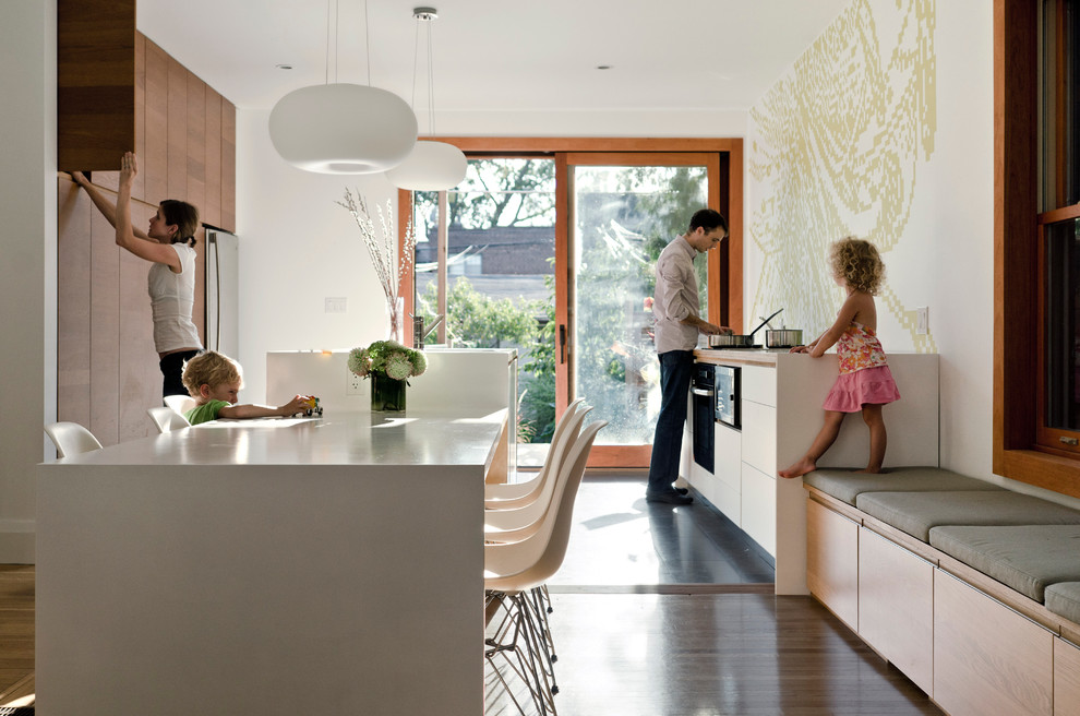 Ejemplo de cocina comedor moderna con electrodomésticos de acero inoxidable, armarios con paneles lisos y puertas de armario de madera en tonos medios