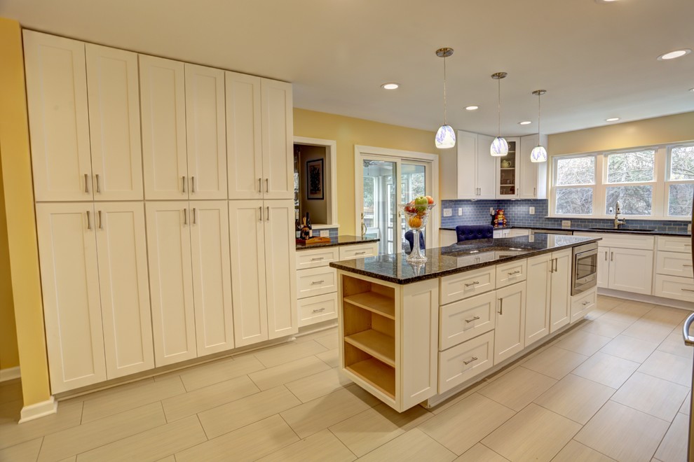 Idéer för ett modernt kök, med en integrerad diskho, luckor med infälld panel, vita skåp, granitbänkskiva, blått stänkskydd, stänkskydd i glaskakel, rostfria vitvaror, travertin golv och en köksö