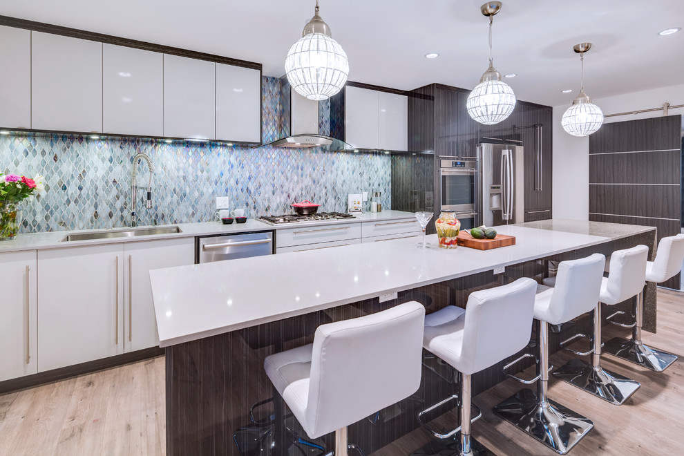 This is an example of a contemporary galley kitchen in Vancouver with a single-bowl sink, flat-panel cabinets, white cabinets, blue splashback, glass tiled splashback, stainless steel appliances, light hardwood flooring, an island and beige floors.