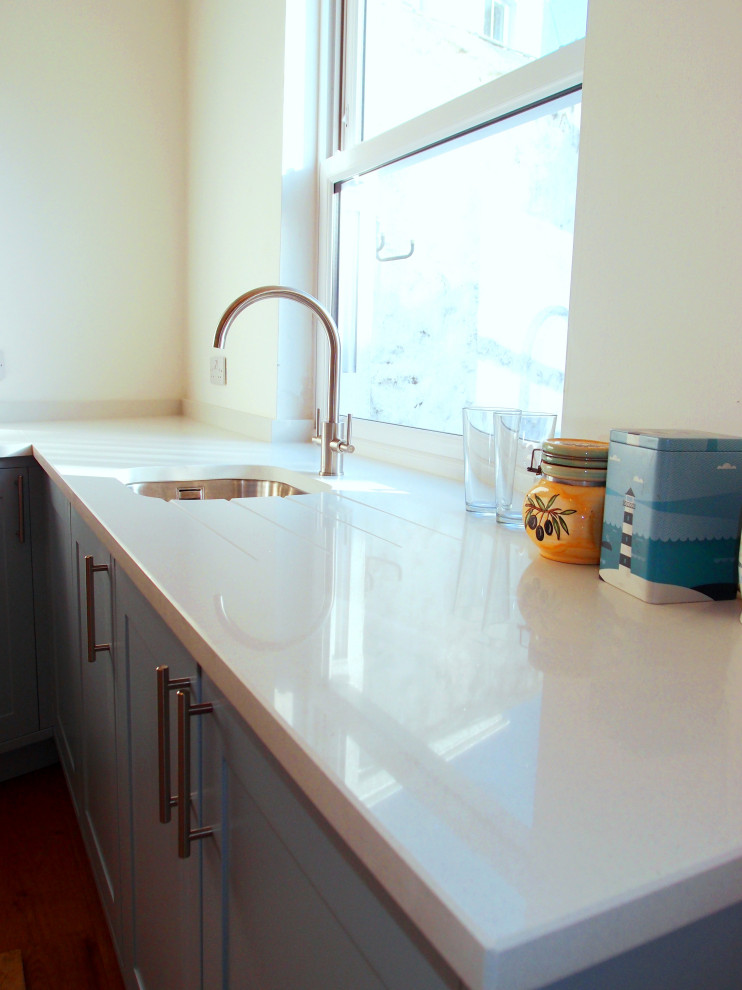Idéer för ett litet modernt vit kök, med en enkel diskho, skåp i shakerstil, blå skåp, bänkskiva i kvarts, rostfria vitvaror, mellanmörkt trägolv och brunt golv