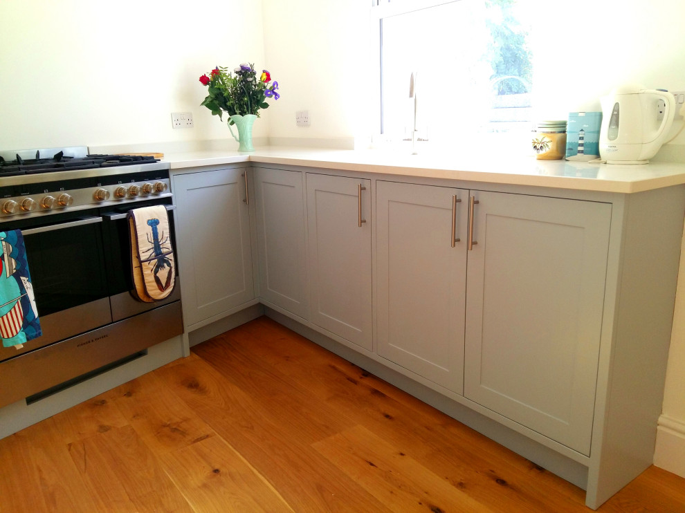 Inredning av ett modernt litet vit vitt kök, med en enkel diskho, skåp i shakerstil, blå skåp, bänkskiva i kvarts, rostfria vitvaror, mellanmörkt trägolv och brunt golv