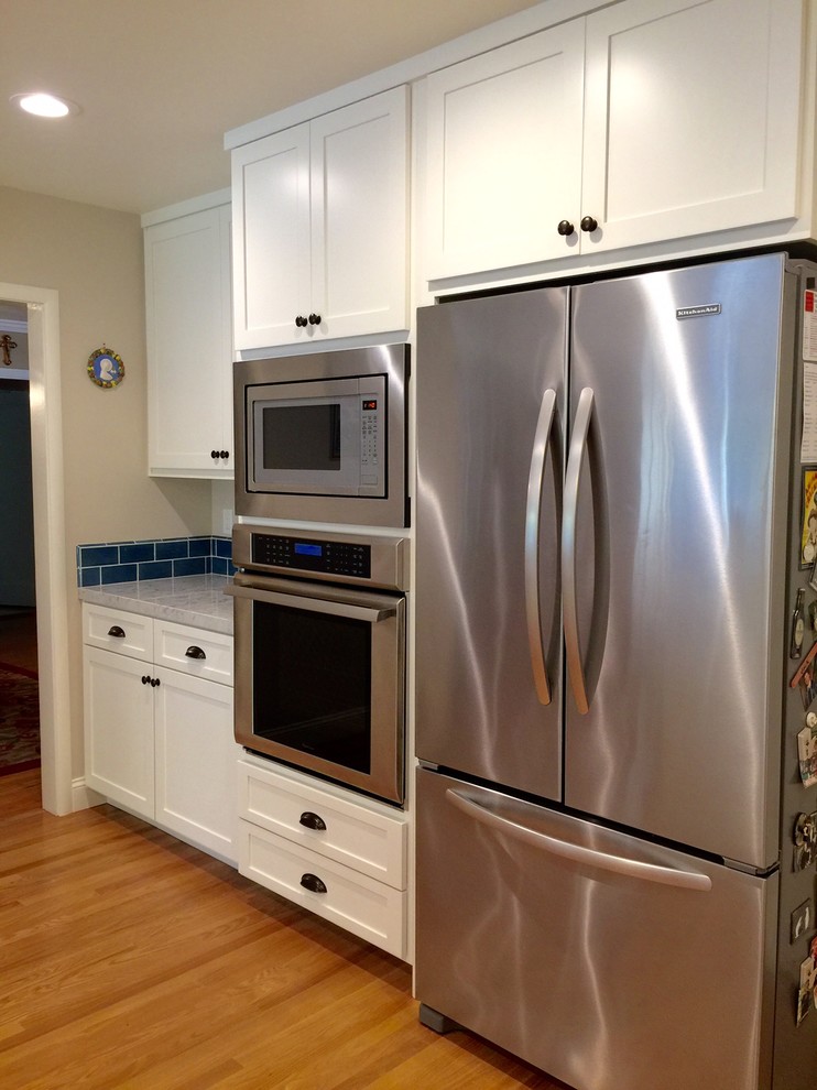 Diseño de cocina de estilo de casa de campo de tamaño medio con armarios con paneles empotrados, salpicadero azul, electrodomésticos de acero inoxidable y suelo de madera en tonos medios