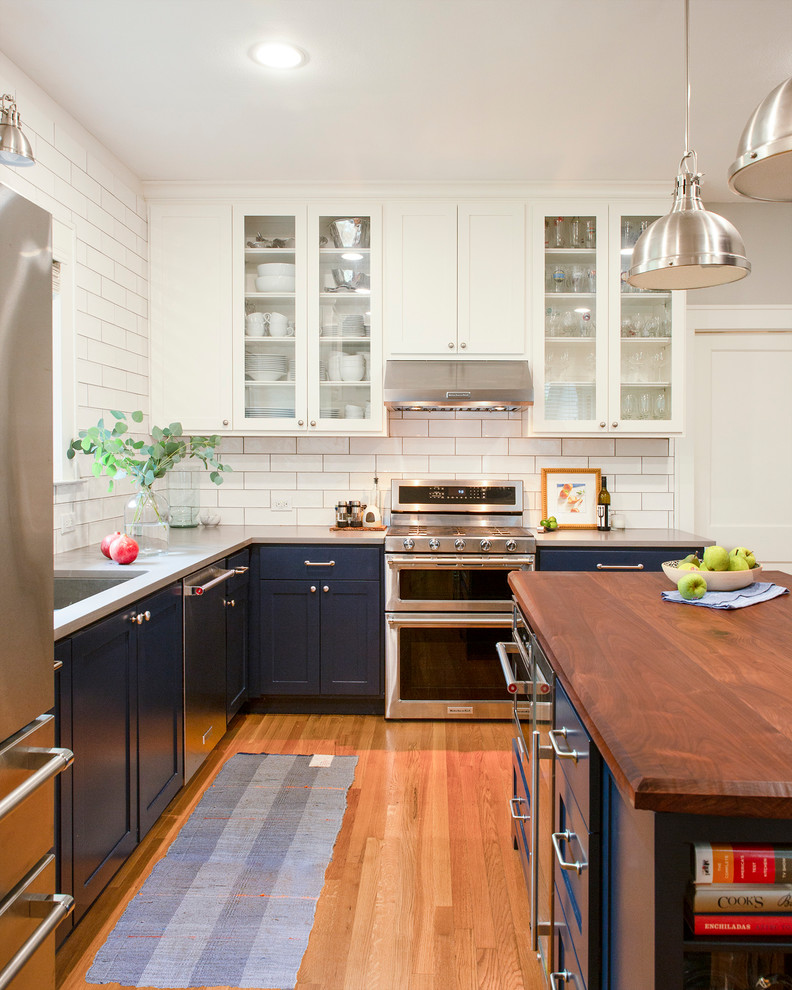 Bild på ett stort lantligt kök, med skåp i shakerstil, blå skåp, vitt stänkskydd, stänkskydd i tunnelbanekakel, rostfria vitvaror och en köksö