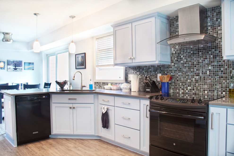 Classic galley enclosed kitchen in Milwaukee with a submerged sink, shaker cabinets, grey cabinets, engineered stone countertops, multi-coloured splashback, glass tiled splashback, black appliances, light hardwood flooring and a breakfast bar.
