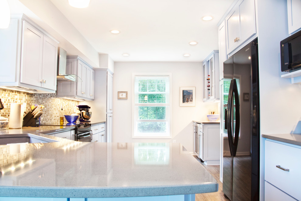 Transitional galley light wood floor enclosed kitchen photo in Milwaukee with an undermount sink, shaker cabinets, white cabinets, quartz countertops, multicolored backsplash, glass tile backsplash, black appliances and a peninsula