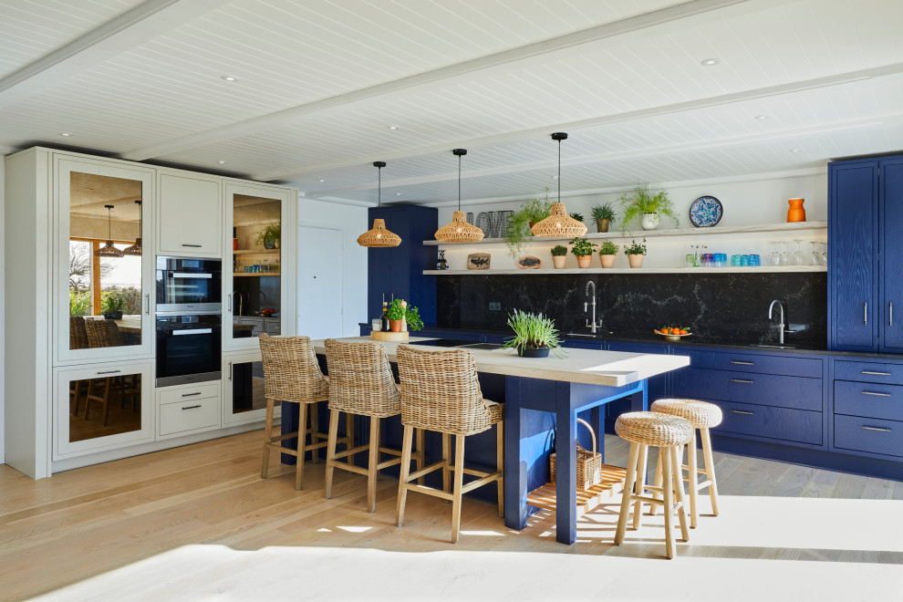 Foto på ett mellanstort maritimt svart linjärt kök med öppen planlösning, med en undermonterad diskho, luckor med profilerade fronter, blå skåp, bänkskiva i kvartsit, svart stänkskydd, rostfria vitvaror, laminatgolv, en köksö och beiget golv