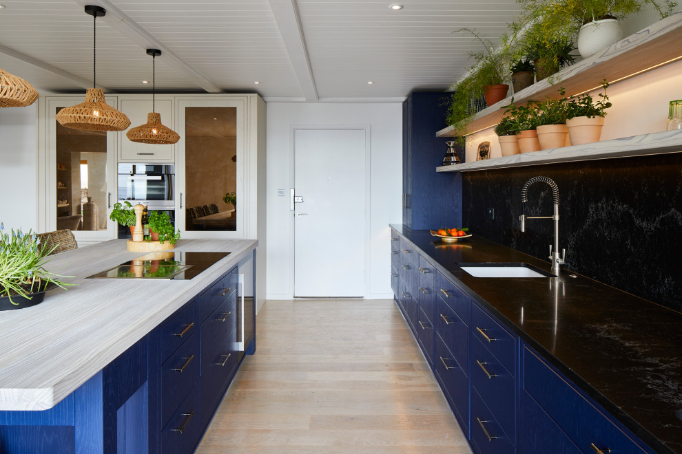 Design ideas for a medium sized coastal single-wall open plan kitchen in Kent with a submerged sink, beaded cabinets, blue cabinets, quartz worktops, black splashback, stainless steel appliances, laminate floors, an island, beige floors and black worktops.