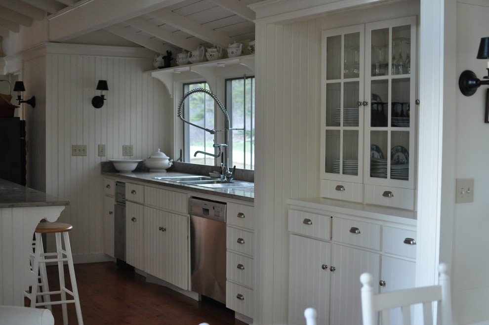 Bild på ett stort lantligt kök, med en dubbel diskho, vita skåp, rostfria vitvaror, mellanmörkt trägolv och en köksö