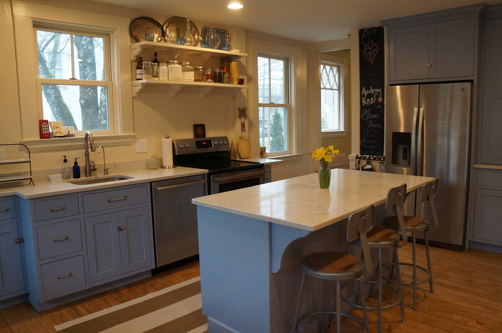 Exempel på ett litet klassiskt kök, med en enkel diskho, skåp i shakerstil, blå skåp, bänkskiva i kvarts, vitt stänkskydd, rostfria vitvaror, ljust trägolv och en köksö