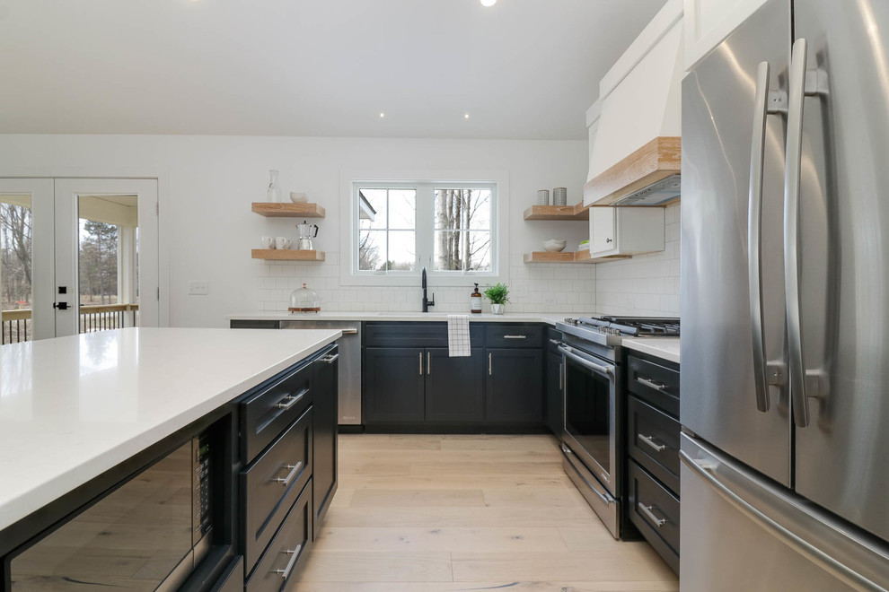 Inspiration for a mid-sized country l-shaped light wood floor and beige floor eat-in kitchen remodel in Grand Rapids with an undermount sink, shaker cabinets, black cabinets, quartz countertops, white backsplash, subway tile backsplash, stainless steel appliances and an island