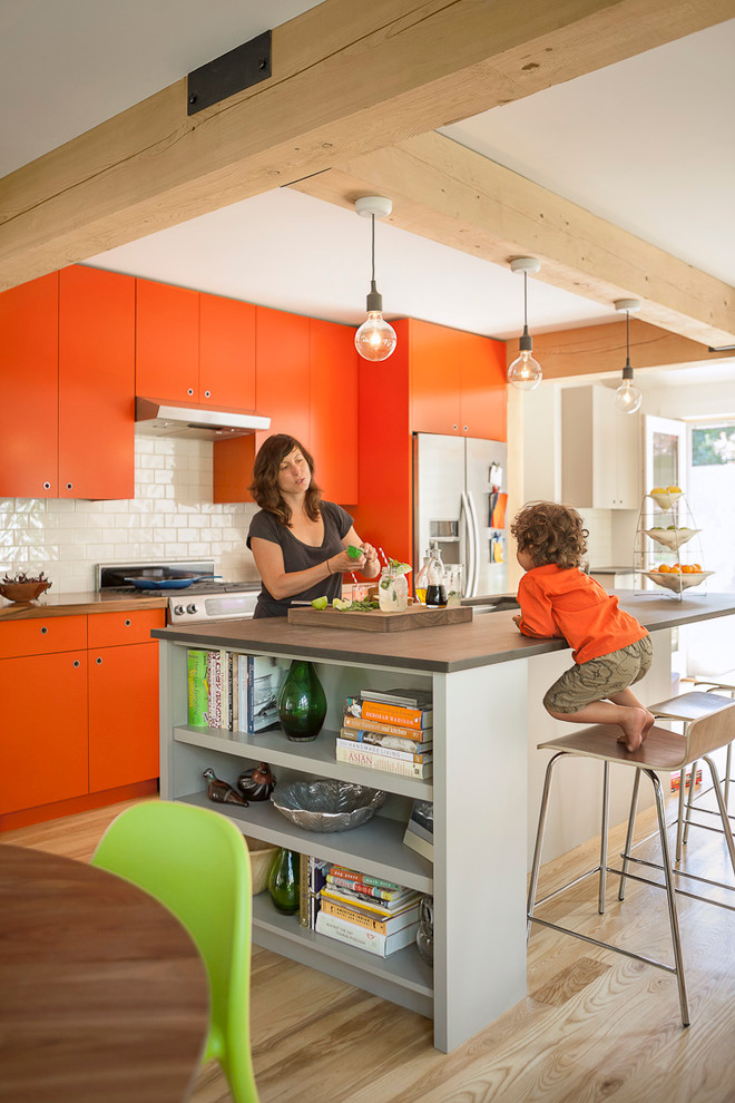 ポートランド(メイン)にあるコンテンポラリースタイルのおしゃれなキッチン (フラットパネル扉のキャビネット、オレンジのキャビネット、白いキッチンパネル、サブウェイタイルのキッチンパネル、シルバーの調理設備) の写真