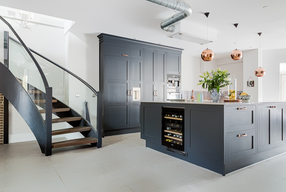 This is an example of a large industrial l-shaped kitchen/diner in London with a belfast sink, shaker cabinets, blue cabinets, quartz worktops, multi-coloured splashback, mosaic tiled splashback, black appliances, concrete flooring, an island and grey floors.