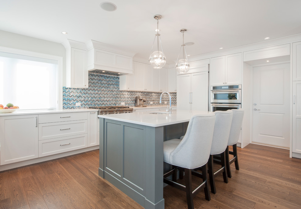 Mid-sized transitional l-shaped medium tone wood floor and brown floor kitchen photo in Vancouver with an undermount sink, shaker cabinets, white cabinets, quartz countertops, paneled appliances, an island, white countertops and multicolored backsplash