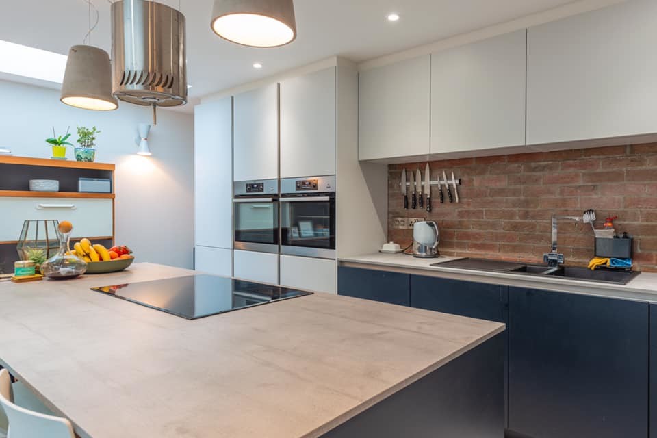 Bild på ett mellanstort funkis grå linjärt grått kök och matrum, med en integrerad diskho, släta luckor, blå skåp, bänkskiva i betong, rött stänkskydd, stänkskydd i tegel, rostfria vitvaror, betonggolv, en köksö och grått golv