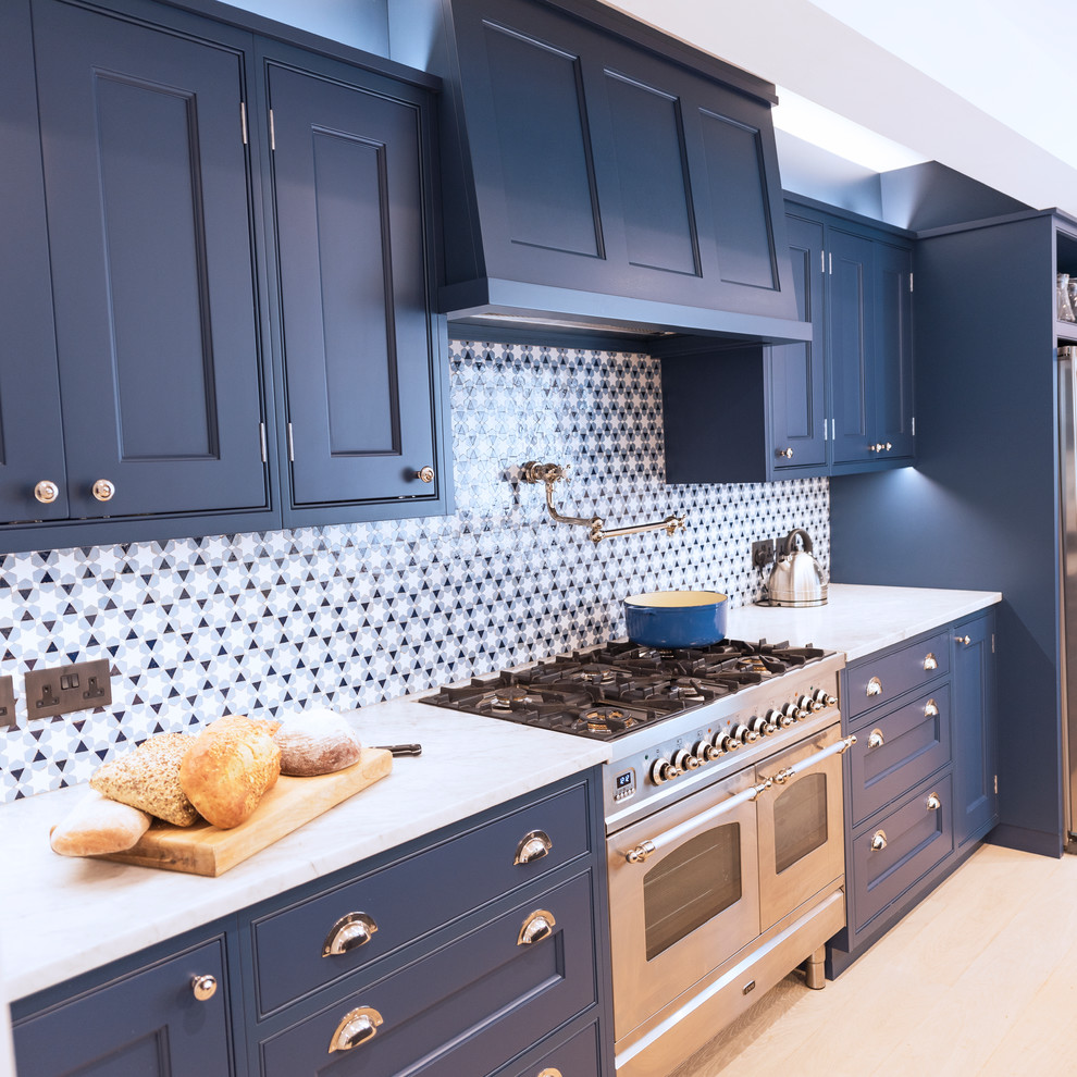 Modern inredning av ett stort beige beige kök, med en rustik diskho, luckor med infälld panel, blå skåp, marmorbänkskiva, blått stänkskydd, rostfria vitvaror, ljust trägolv, en köksö och beiget golv