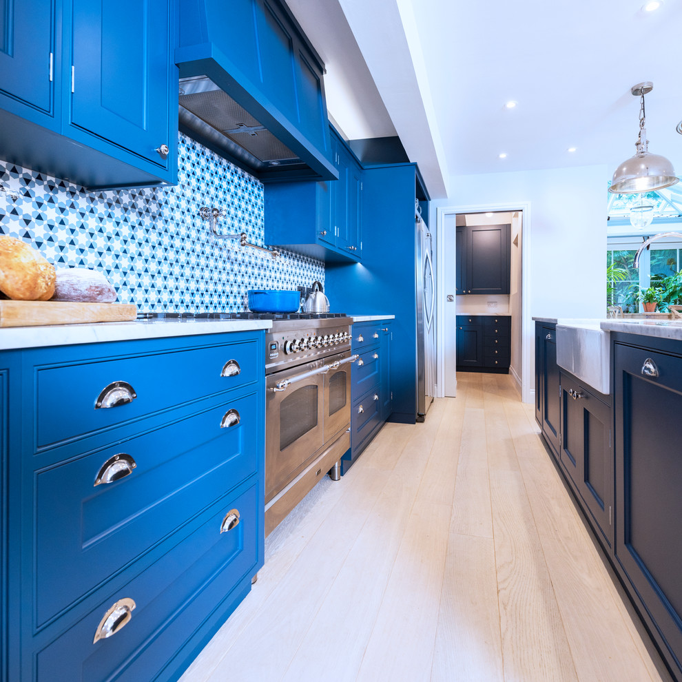 Bild på ett stort funkis vit vitt kök, med en rustik diskho, luckor med infälld panel, blå skåp, marmorbänkskiva, flerfärgad stänkskydd, rostfria vitvaror, ljust trägolv, en köksö och vitt golv