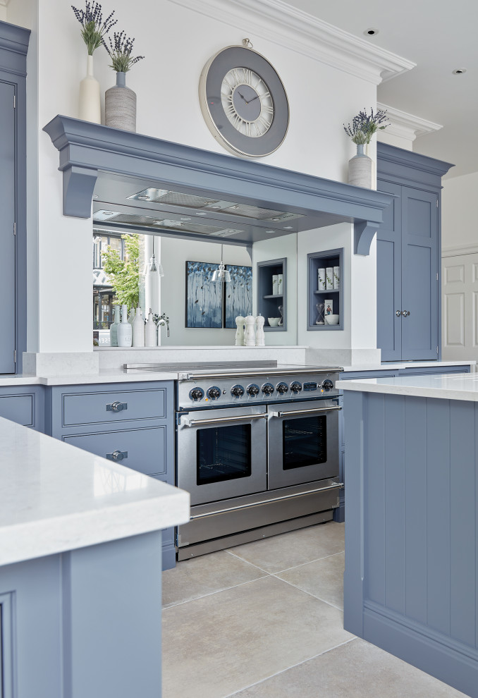 Klassisk inredning av ett stort vit vitt kök, med en undermonterad diskho, skåp i shakerstil, blå skåp, bänkskiva i kvarts, vitt stänkskydd, spegel som stänkskydd, rostfria vitvaror, kalkstensgolv, flera köksöar och beiget golv