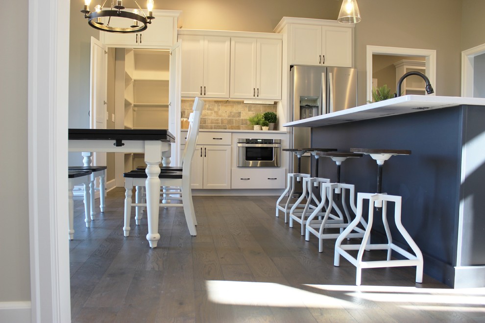 Minimalistisk inredning av ett stort vit vitt kök, med en undermonterad diskho, släta luckor, blå skåp, bänkskiva i kvarts, beige stänkskydd, stänkskydd i porslinskakel, rostfria vitvaror, mellanmörkt trägolv, en köksö och grått golv