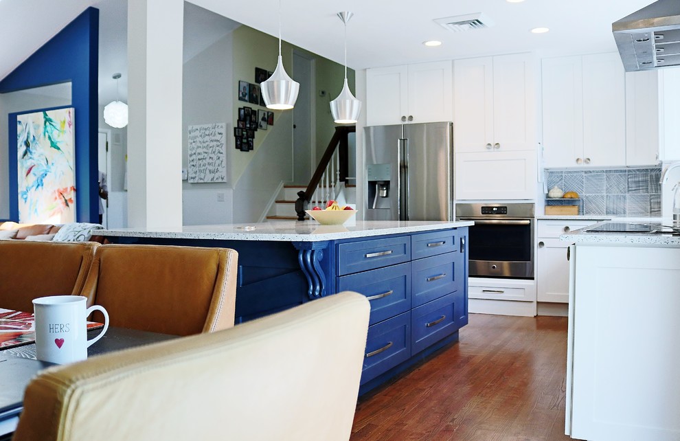 Photo of a medium sized classic l-shaped kitchen/diner in New York with a belfast sink, shaker cabinets, blue cabinets, engineered stone countertops, blue splashback, glass tiled splashback, stainless steel appliances, light hardwood flooring, an island, brown floors and white worktops.