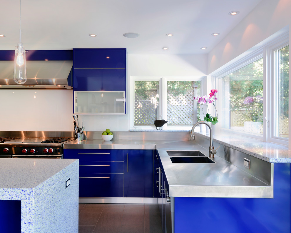 Exemple d'une cuisine tendance avec un évier intégré, un placard à porte plane, des portes de placard bleues, un plan de travail en inox, une crédence en feuille de verre et un électroménager en acier inoxydable.