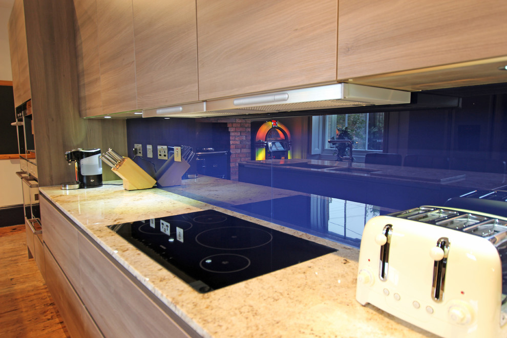 Idée de décoration pour une grande cuisine design en bois clair avec une crédence bleue, une crédence en feuille de verre et îlot.