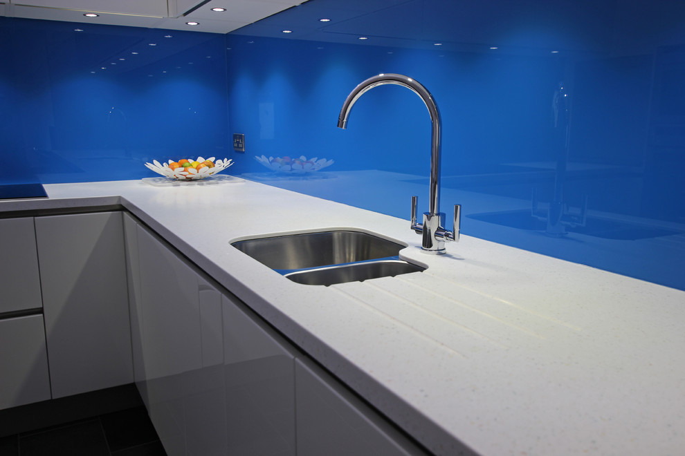 Bild på ett funkis kök, med vita skåp, blått stänkskydd, glaspanel som stänkskydd och en köksö