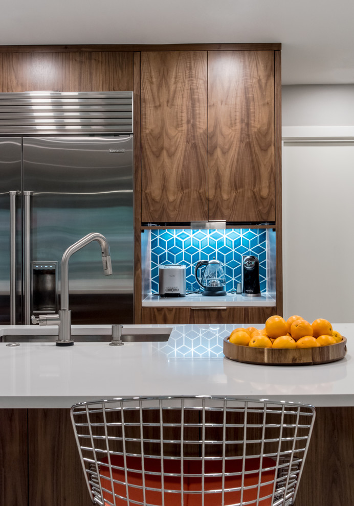 Photo of a medium sized retro l-shaped kitchen/diner in Austin with medium wood cabinets, blue splashback, ceramic splashback, stainless steel appliances, an island, beige floors and grey worktops.
