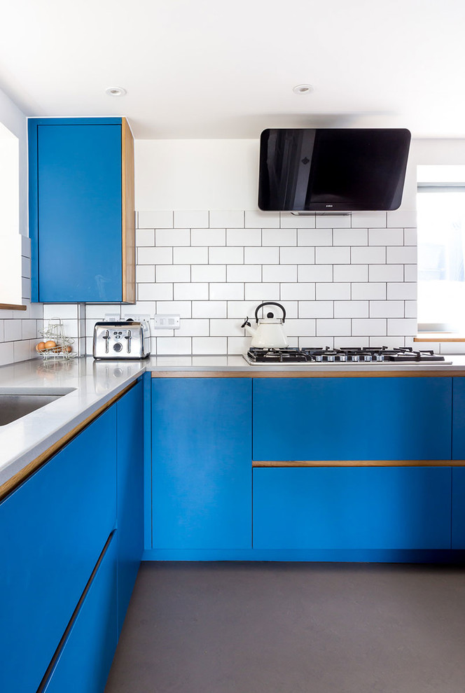 This is an example of a medium sized contemporary u-shaped kitchen/diner in Wiltshire with a submerged sink, flat-panel cabinets, blue cabinets, white splashback, stone tiled splashback, stainless steel appliances, concrete flooring and no island.