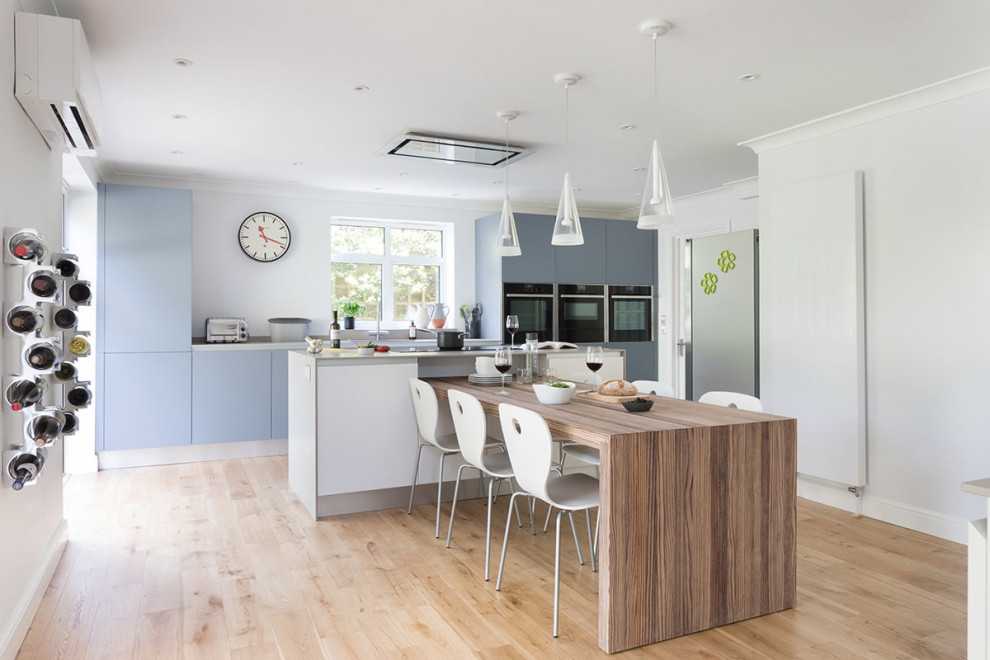 Inspiration for a large contemporary galley kitchen/diner in London with flat-panel cabinets, blue cabinets, laminate countertops, black appliances, laminate floors, an island, grey worktops and beige floors.