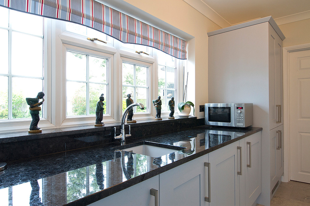 Medium sized traditional l-shaped kitchen/diner in Buckinghamshire with a built-in sink, granite worktops, grey splashback, glass sheet splashback, integrated appliances, ceramic flooring, no island, shaker cabinets and blue cabinets.