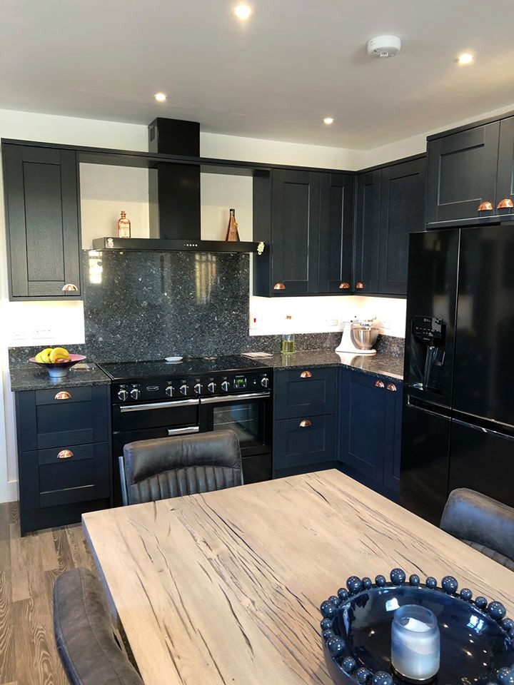Modern l-shaped kitchen in West Midlands with blue cabinets, granite worktops, blue splashback, black appliances and blue worktops.